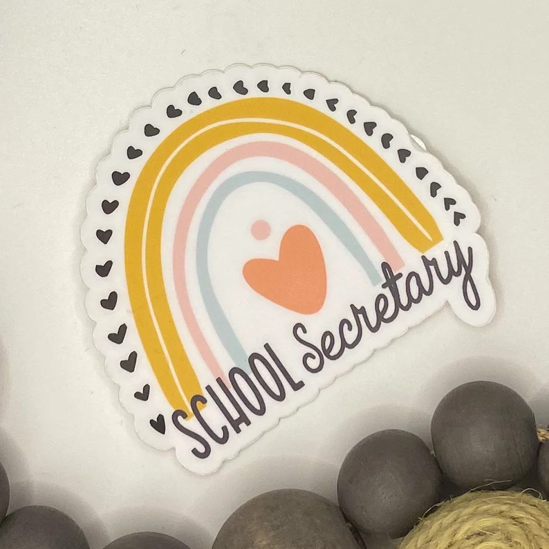 A sticker has a rainbow and heart on it and it says "school secretary" (gifts for paraprofessionals)