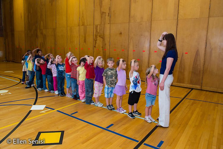 young students line up in front of their teacher inside of a gym, as an example of team-building games and activities