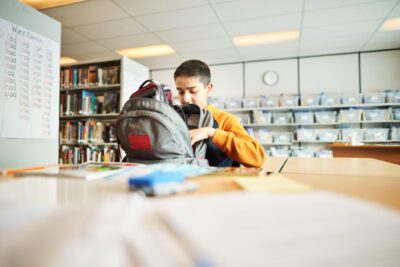 Shot of a boy packing his schoolbag sitting in classroom