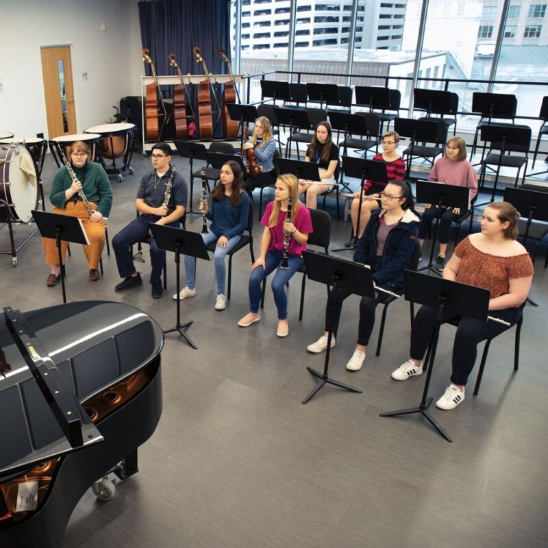 Middle school students seated on student chairs and playing instruments in music classroom