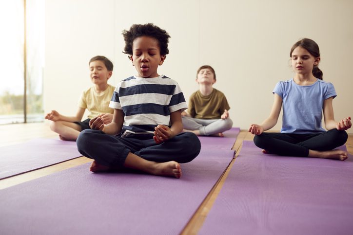 Group of children sitting on exercise mats and meditating in yoga studio, as an example of SEL activities