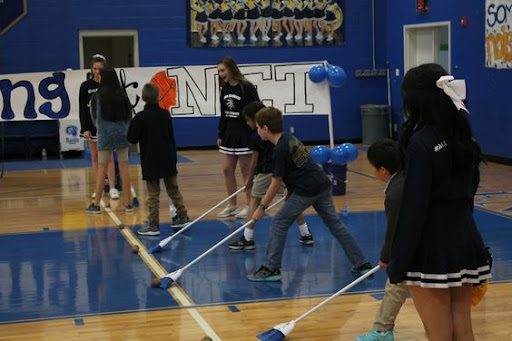 Student sweeping a potato across gym floor