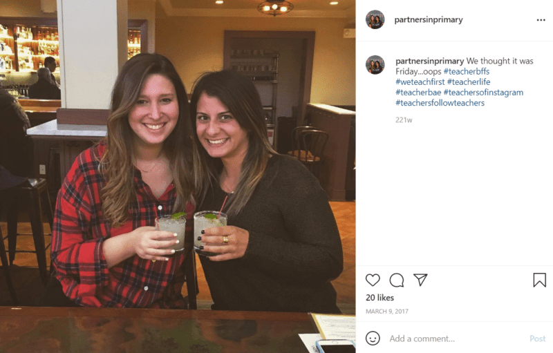 Two teachers pose together at a bar/restaurant holding cocktails