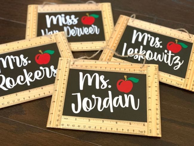 Black chalkboard signs framed with wooden rules with teacher names and apple printed on the sign