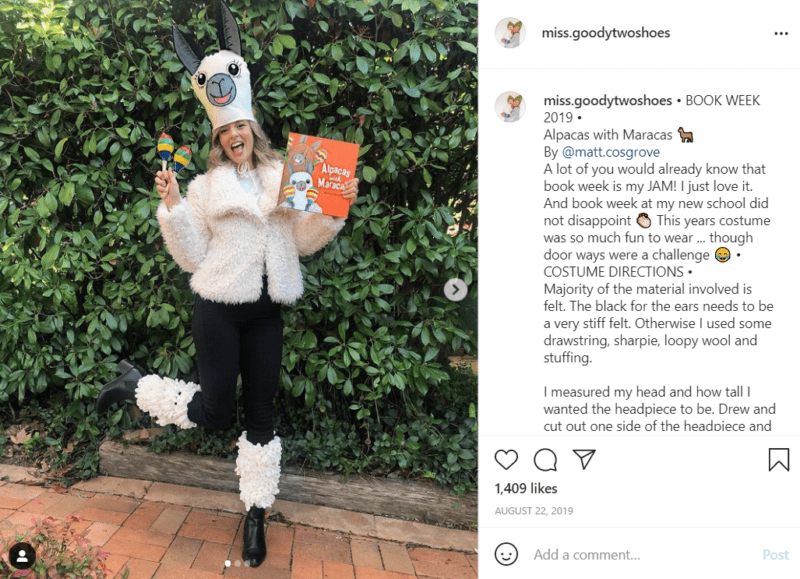 Teacher outside in front of a shrub dressed as an alpaca holding a copy of the books Alpacas with Maracas