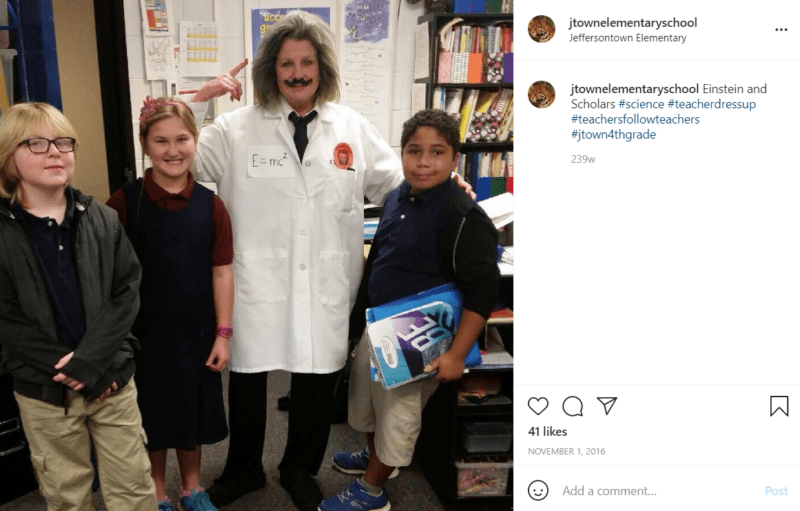 Teacher dressed up as Albert Einstein surrounded by three students in a classroom