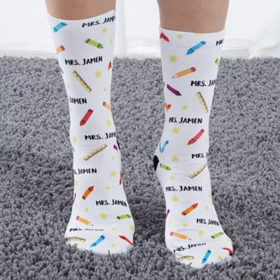 Feet are shown wearing white socks with crayons on them and pencils that have a teacher's name on them.