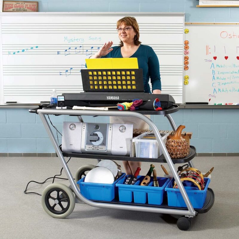 Music teacher in classroom standing behind TeacherTAXI Cartfilled with music education products