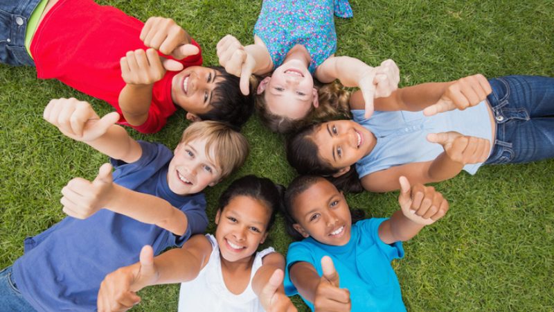 group of school kids lying in a circle on the grass