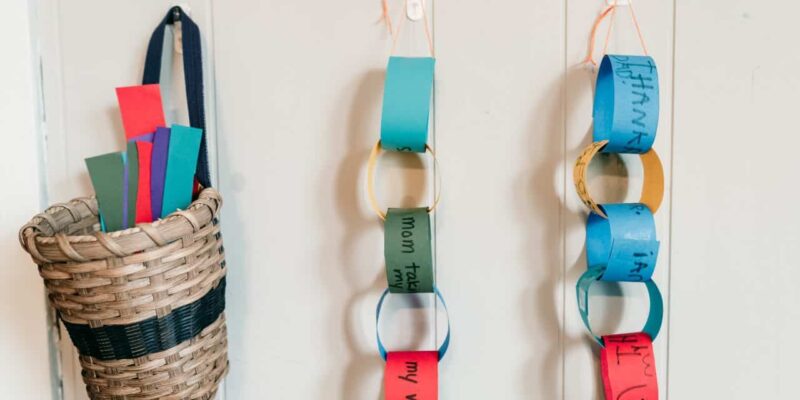 (Gratitude Activities for Kids) Construction paper loops are glued together to form a long chain. Strips of paper are in a basket beside the chains.