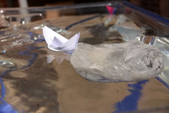 Bote de papel flotando en un plato con un gran trozo de hielo