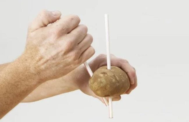 Man's hand stabbing a sweet potato with a drinking straw 