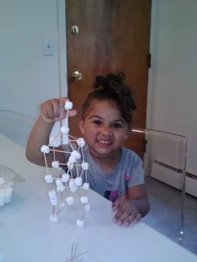 little girl in the classroom showing off her tower made from toothpicks and tiny marshmallows, as an example of team-building games and activities