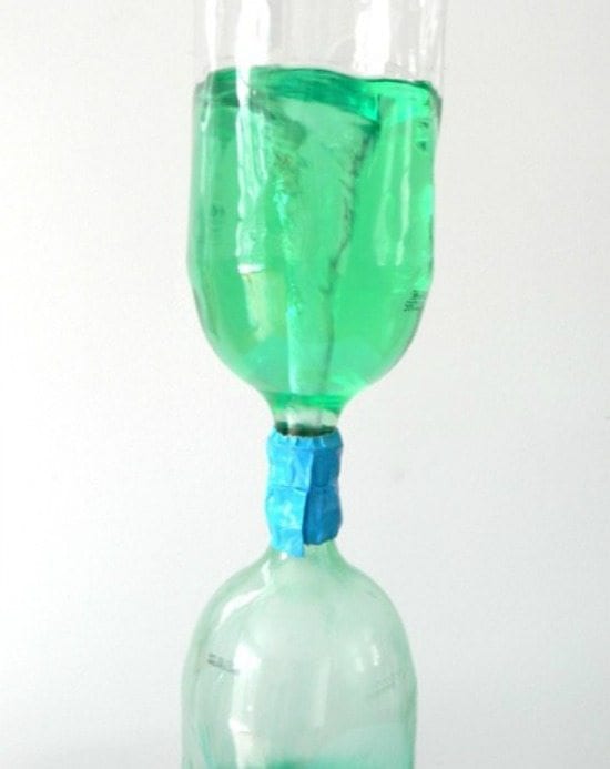 two liter soda bottles duct taped together at the mouths. green liquid from top bottle is swirling down into bottom bottle