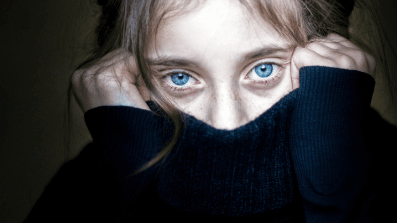 close up of traumatized girl with bright blue eyes covering mouth and nose with sweater during trauma informed teaching