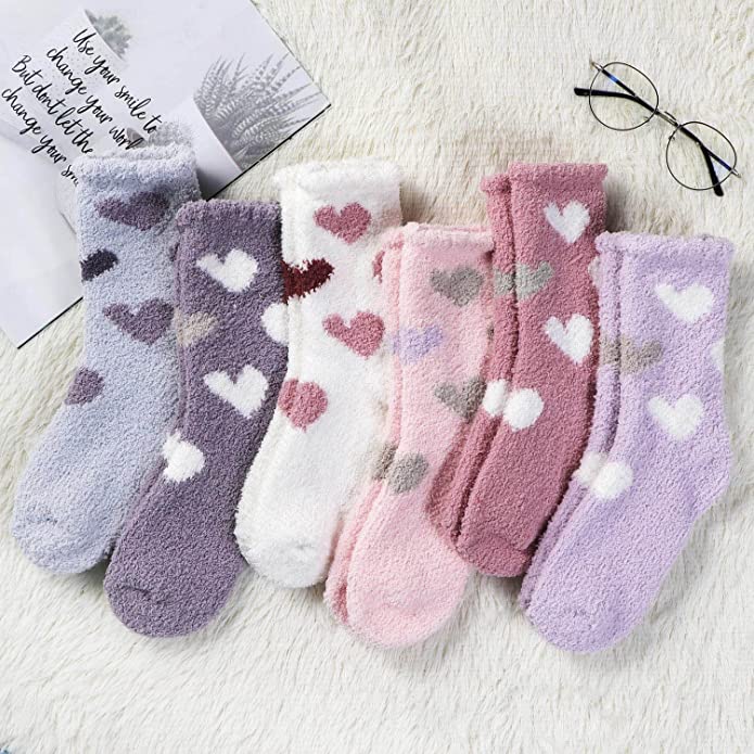 Six pairs of fuzzy heart socks with a note and glasses on a rug, as an example of teacher valentine gift.