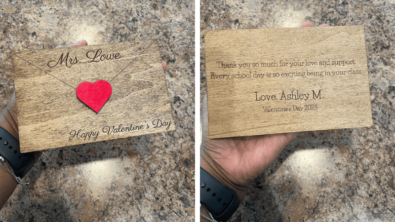 Hand holding front and back of engraved wooden teacher valentine that looks like an envelope.