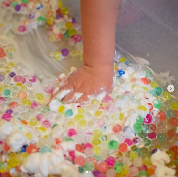 Child's hand in a sensory table filled with multicolored water beads and shaving cream