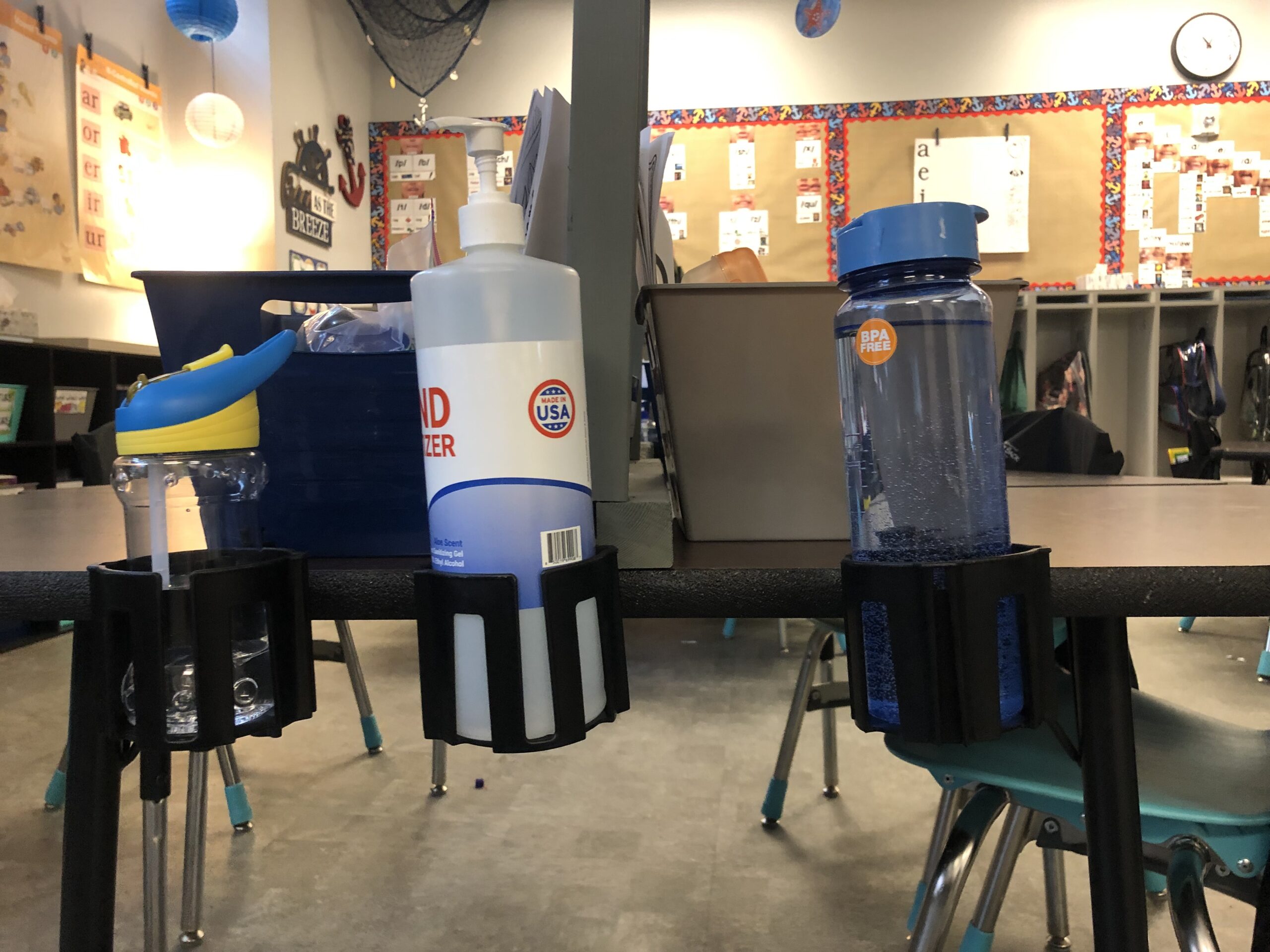 Cup Holster bottle holder attached to classroom desk, holding water bottle and cleaning wipes (Water Bottle Holders for Student Desks)