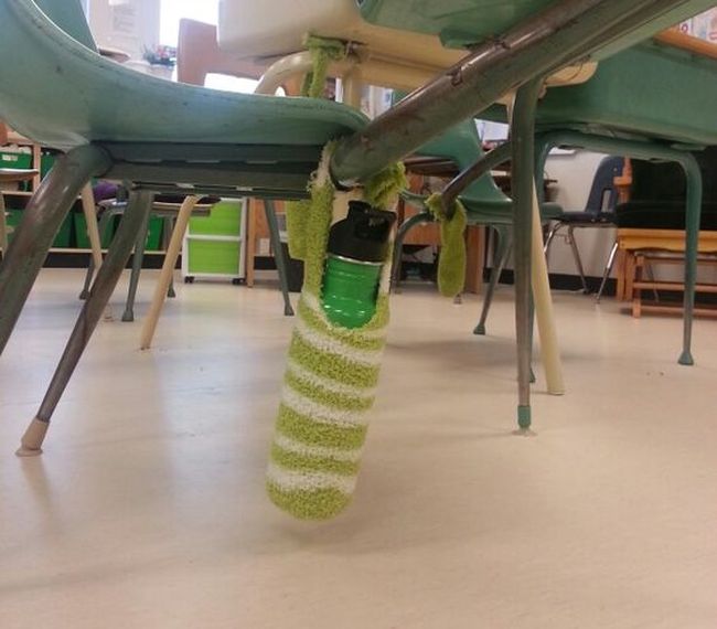 Green striped fuzzy sock cut and tied to be a water bottle holder attached to a student desk