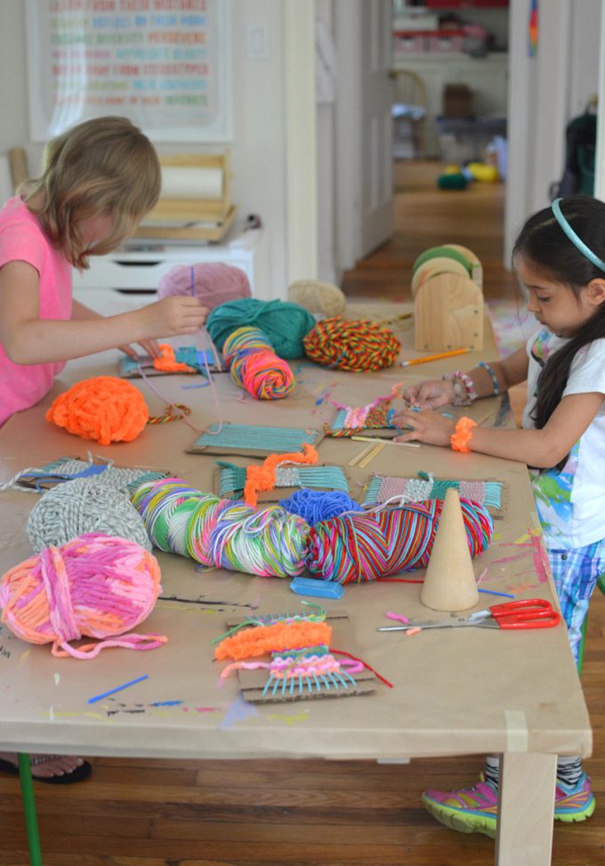 two girls weaving with yarn at a table