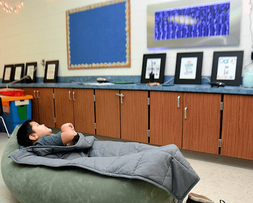 Child laying under a weighted blanket in a classroom
