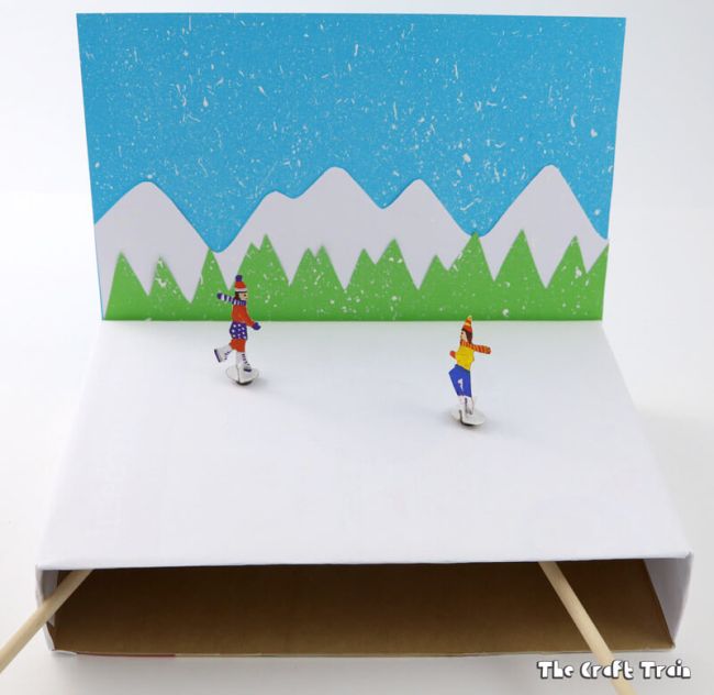 Cardboard figure skating rink with miniature skaters controlled by magnets