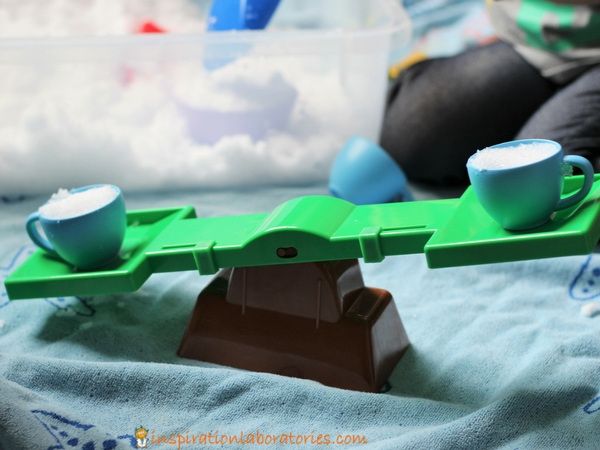 Child using a toy scale to compare two cups of snow (Winter Science)