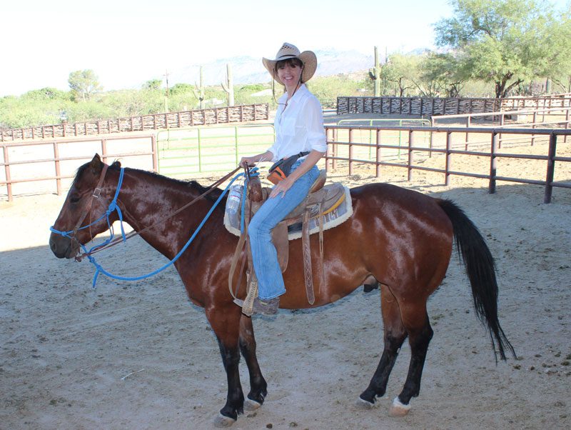 A woman is shown smiling while riding a horse 