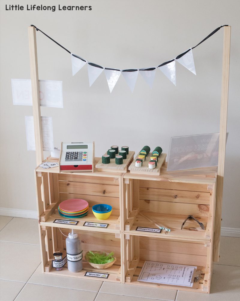 Four wooden crates are assembled to form a toy farm stand. A cash register and some fake food are included, , as an example of IKEA classroom supplies.